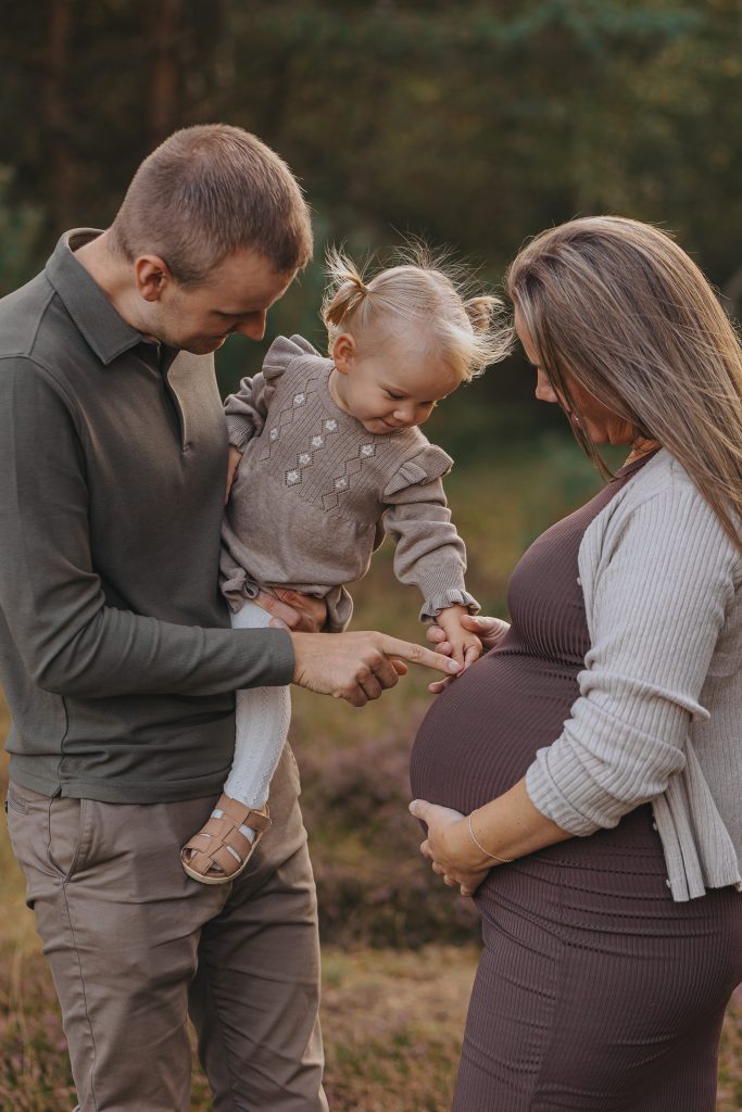 Gravidfotografering utomhus med familj och syskon där barnet möter gravidmagen – naturlig familjefotografering i Skåne